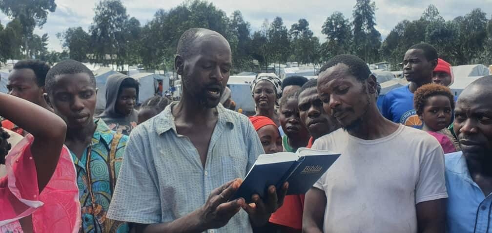 NCE ministers praying with a family among tents at a displacement camp